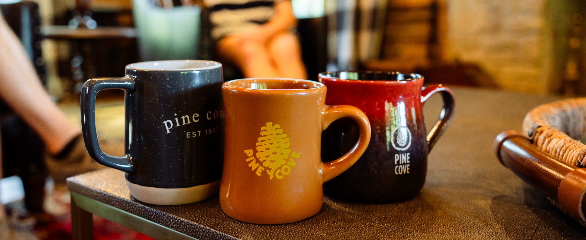 Three Pine Cove mugs lined up on a coffee table in a luxurious cabin setting.